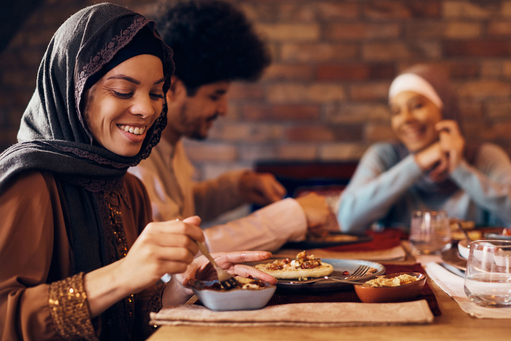 Happy woman from the Middle East eating Ramadan Iftar with her family at the dinner table.